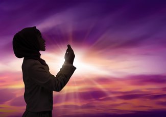 Silhouette of young muslim woman praying to god in sunset background
